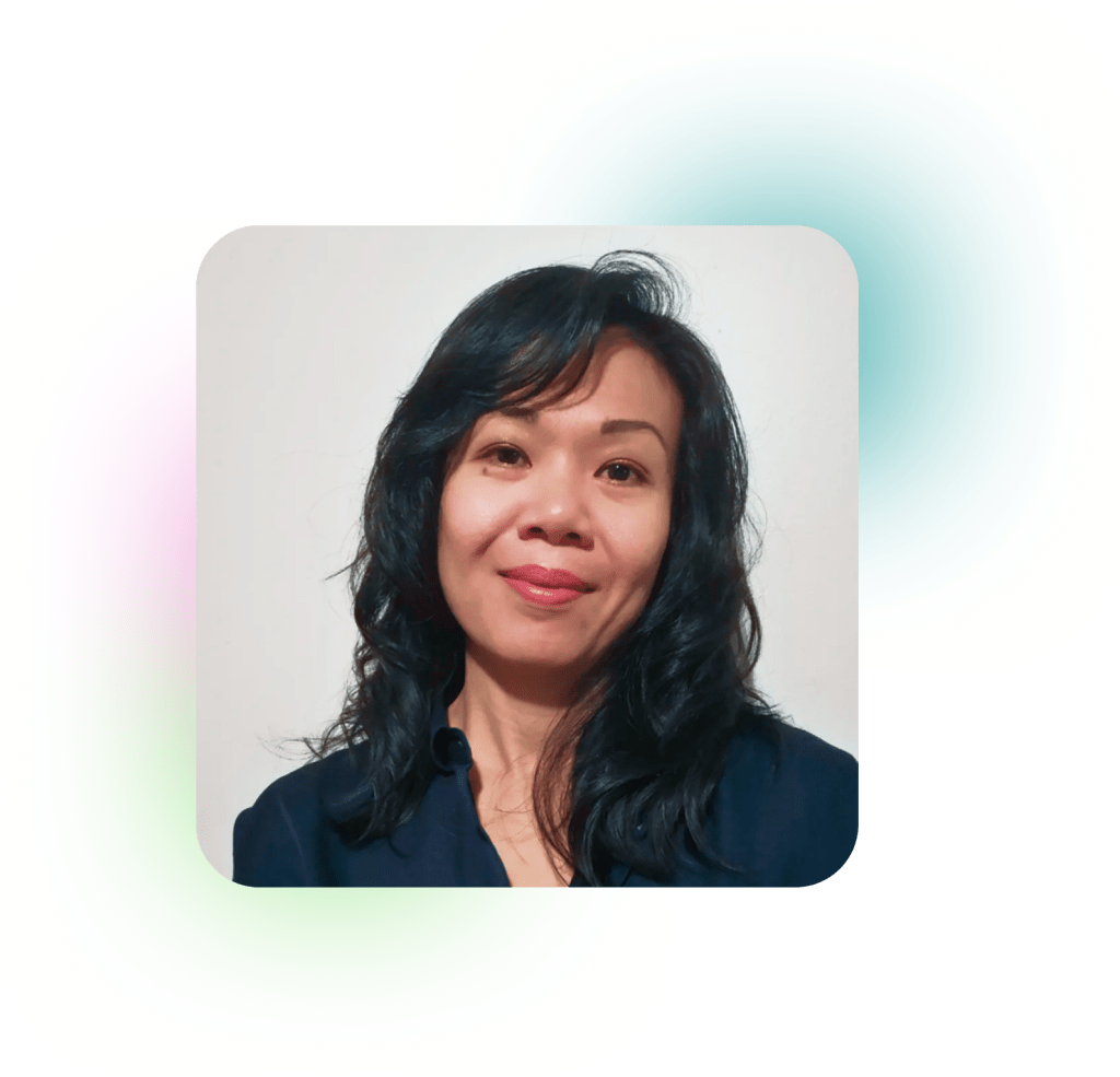 South East Asian person with shoulder length hair and a black v-neck shirt smiling at the camera.